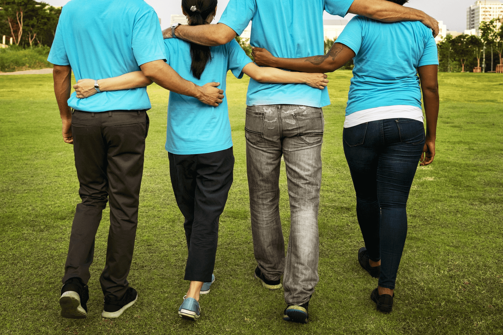 This image depicts the backs of four members of a small nonprofit  with their arms around. Representing the unity of small nonprofits